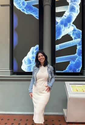 Photo of Oya standing in front of a large screen displaying a DNA strand