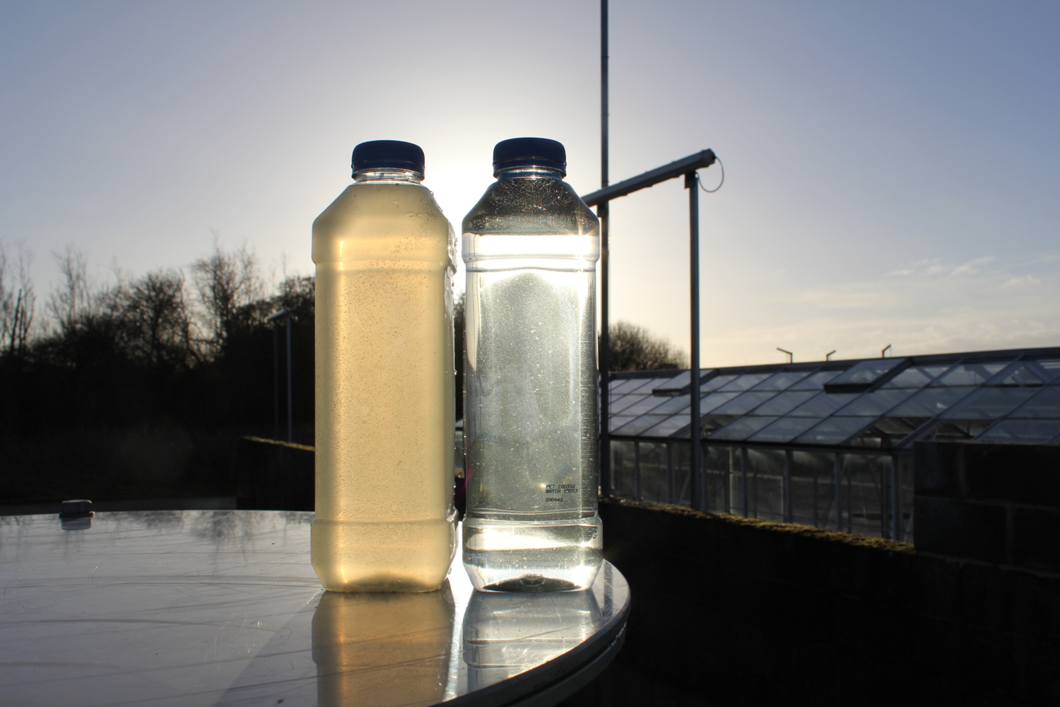 Two bottles of liquid on a table outside over looking warehouse.