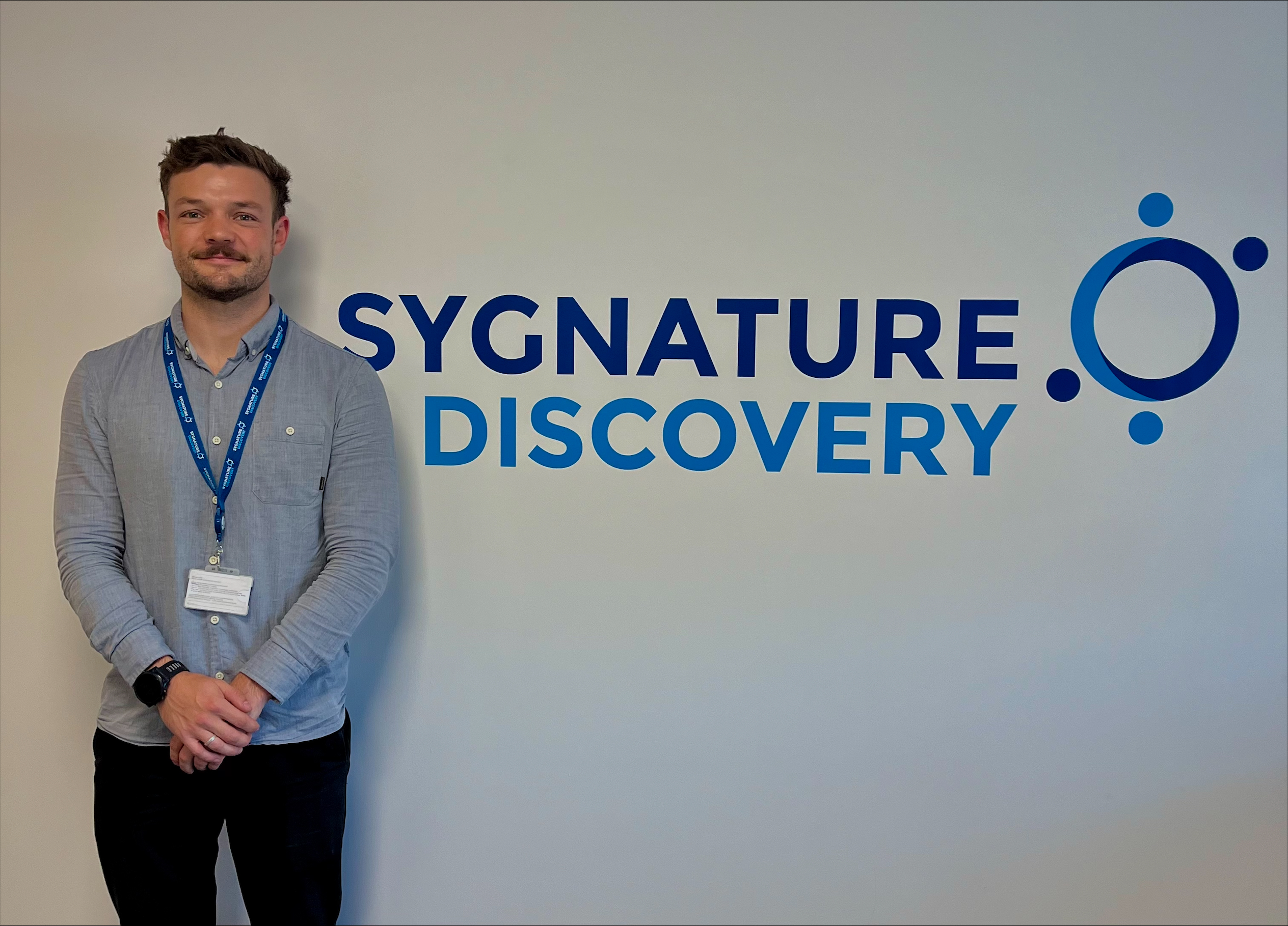 Callum standing next to Sygnature Discovery sign